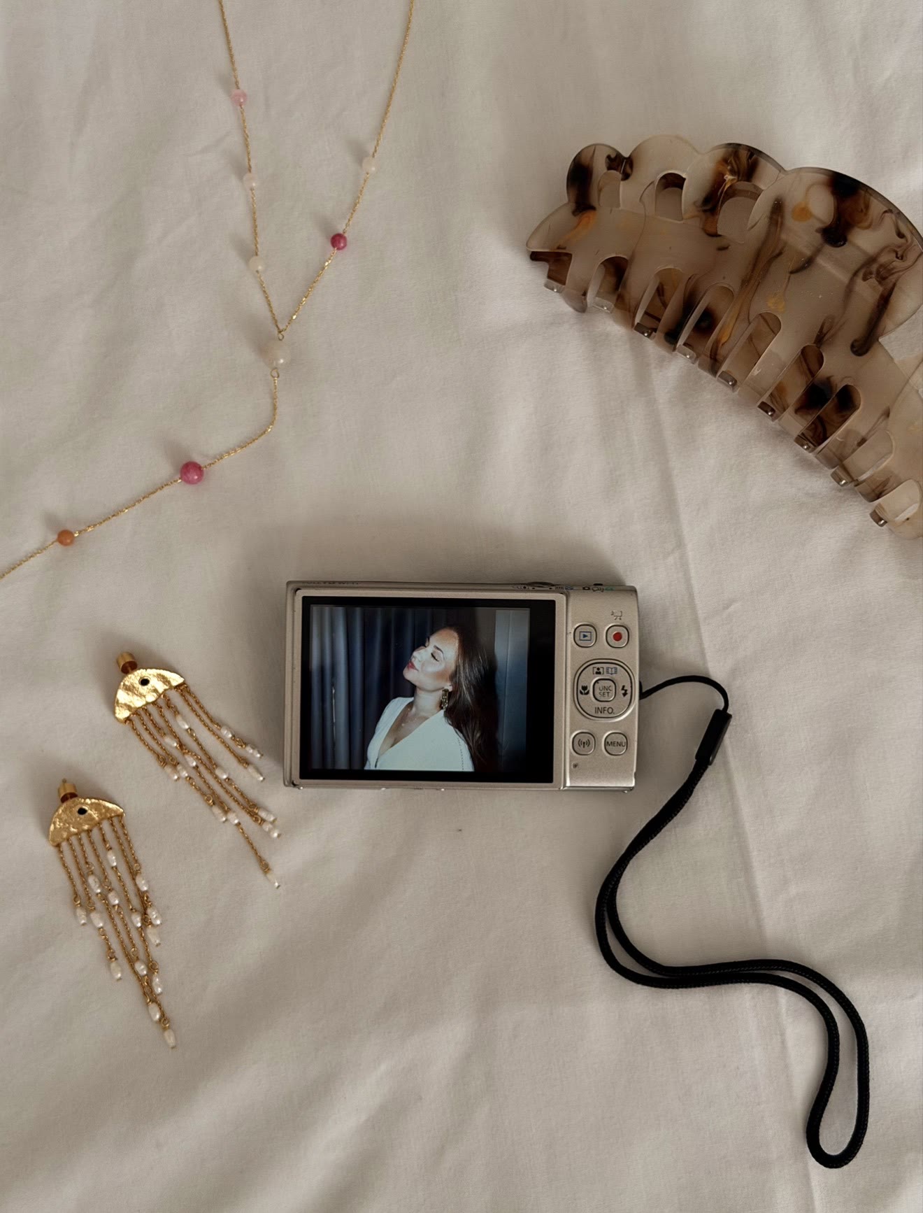 Digital camera and jewelry arranged on a bed